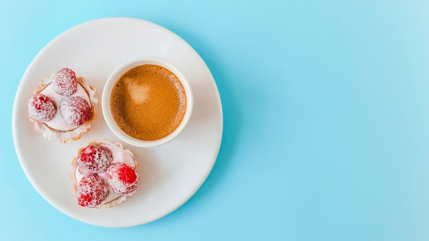 파란색 배경 위에 접시에 나무 딸기와 커피 컵으로 만든 과일 타르트