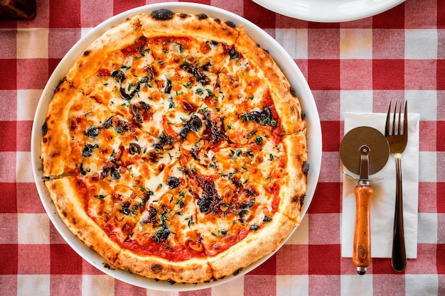 Домашняя итальянская пицца с вялеными помидорами, сыром моцарелла, каперсами и специями на скатерти Вид сверху с копией пространства для текста Столовые приборы на столе на столе