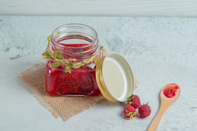 Homemade jam and fresh raspberry on grey surface.