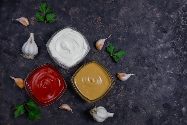 Free photo homemade ketchup,mustard and mayonnaise sauce and ingredients on dark . top view