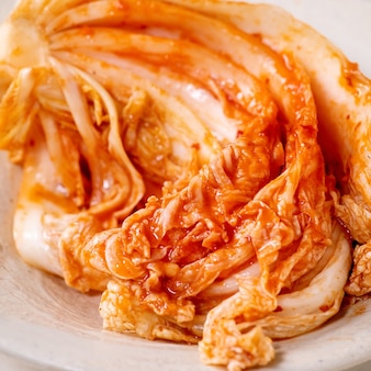 Домашняя корейская традиционная ферментированная капуста кимчи с закусками подается в керамической тарелке на белом мраморном фоне. закройте вверх. квадратное изображение