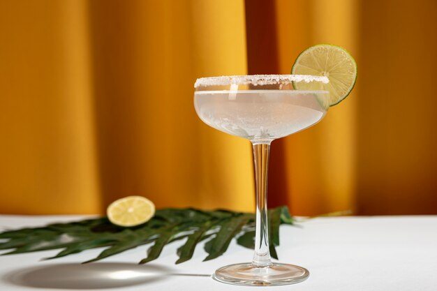 Homemade margarita drink with lime and palm leaf on table against yellow curtain