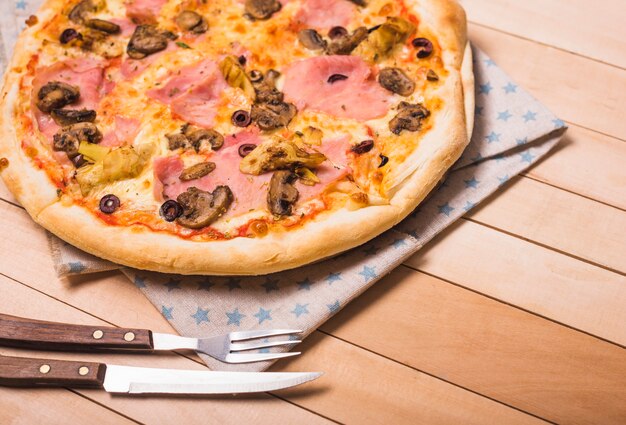 Homemade meat and mushroom pizza on wooden table with fork and knife