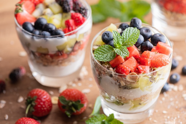 Homemade muesli, bowl of oat granola with yogurt, fresh blueberries, mulberry, strawberries, kiwi, mint and nuts board for healthy breakfast, copy space. Healthy breakfast concept. Clean eating.