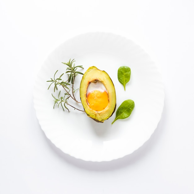 Free photo homemade organic egg baked in avocado with leaves on white background