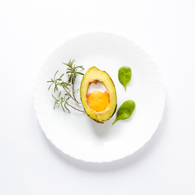 Домашнее органическое яйцо, запеченное в авокадо с листьями на белом фоне