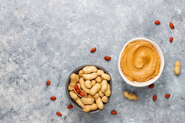 Homemade peanut butter with peanuts on grey concrete table, top view