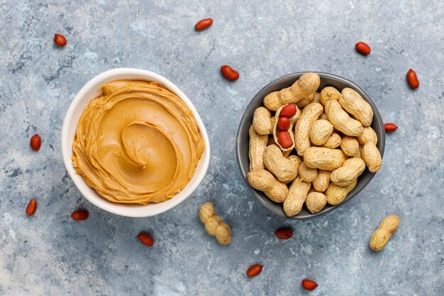 Homemade peanut butter with peanuts on grey concrete table, top view