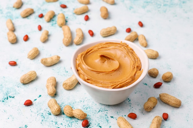 Homemade peanut butter with peanuts on grey concrete table, top view