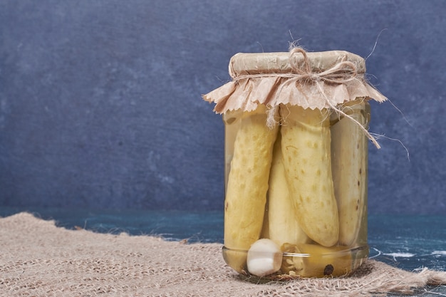 Homemade pickled cucumbers in glass jar on blue with wool tablecloth. 