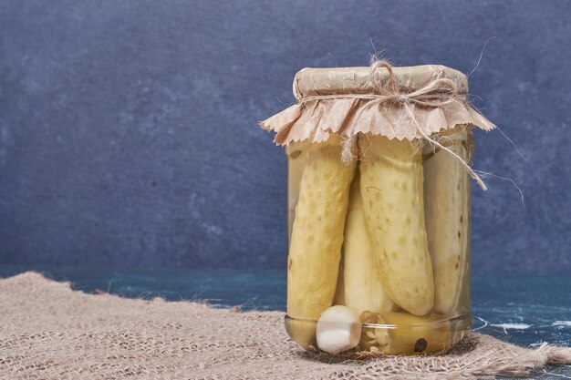 Homemade pickled cucumbers in glass jar on blue with wool tablecloth. 