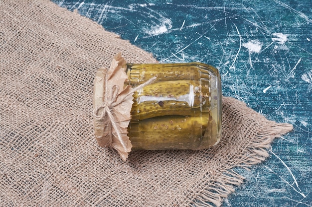 Homemade pickled cucumbers in glass jar on blue with wool tablecloth. 