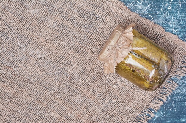 Homemade pickled cucumbers in glass jar on blue with wool tablecloth. 