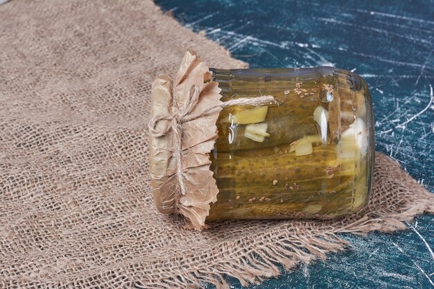 Homemade pickled cucumbers in glass jar on blue with wool tablecloth. 