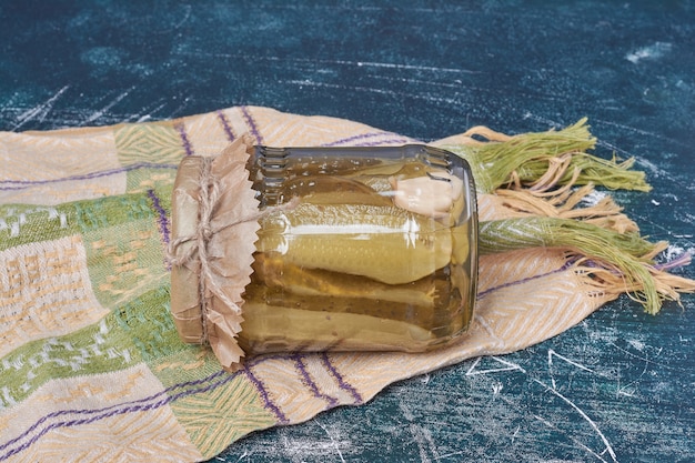 Homemade pickled cucumbers in glass jar on blue with wool tablecloth. 