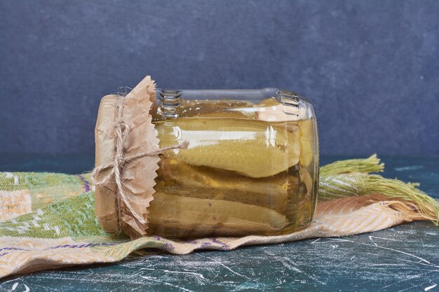 Homemade pickled cucumbers in glass jar on blue with wool tablecloth. 