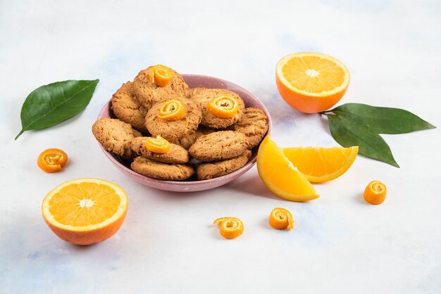 Homemade pile of cookies in pink bowl and orange sliced or half cut over white surface.