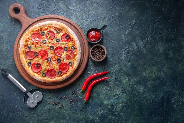 Homemade pizza on wooden cutting board and pepper ketchup on the right side on isolated dark surface