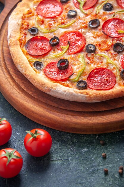 Homemade pizza on wooden cutting board and tomatoes on isolated dark surface