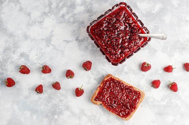 Homemade raspberry jam with fresh raspberries on concrete , top view