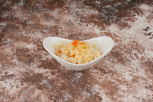 Homemade sauerkraut in a white bowl on marble table. 