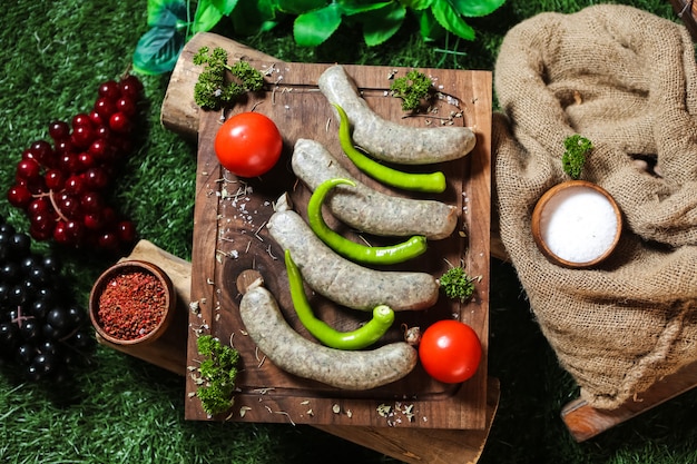 Homemade sausages on the wooden board pepper tomato greens salt