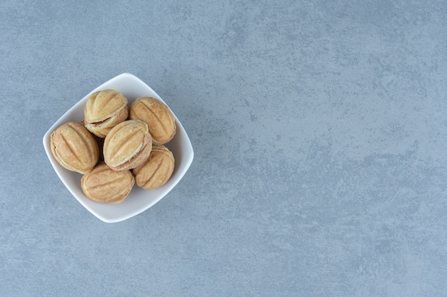 Homemade small cookies form of walnuts in white bowl over grey.