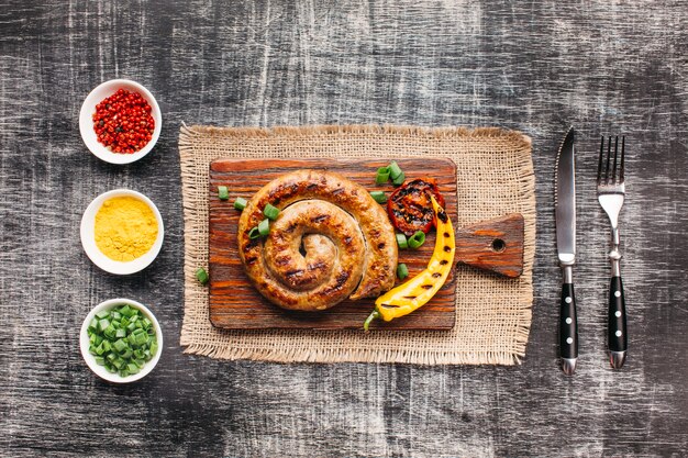 Homemade spiral grilled sausages on cutting board near healthy ingredient arranged in row