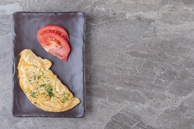 Homemade tasty omelette with tomato on dark plate.
