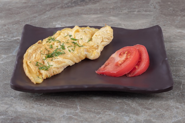 Homemade tasty omelette with tomato on dark plate.