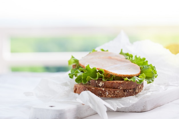 Домашнее вкусный бутерброд с листьями салата и ветчиной на разделочной доске