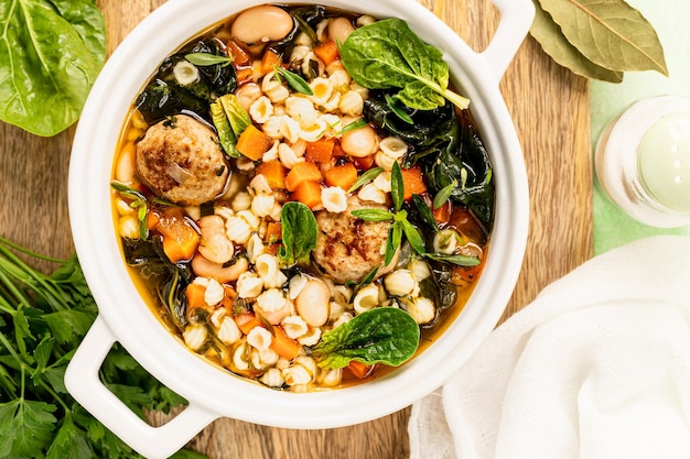 Foto gratuita zuppa di verdure casalinga con polpette e spinaci in una padella bianca su uno sfondo verde