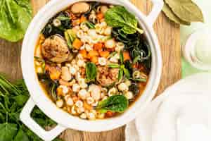 Free photo homemade vegetable soup with meatballs and spinach in a white saucepan on a green background