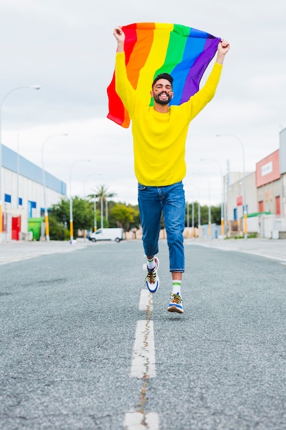 Homosexual running down road holding LGBT flag over head