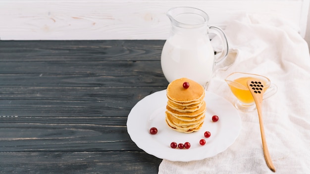 Бесплатное фото Миска для меда; банку молока и стопку блинов на тарелке на деревянном фоне