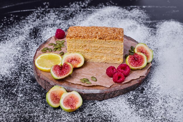 Honey cake decorated with figs, berries and lemon slice in the center of dark table. 