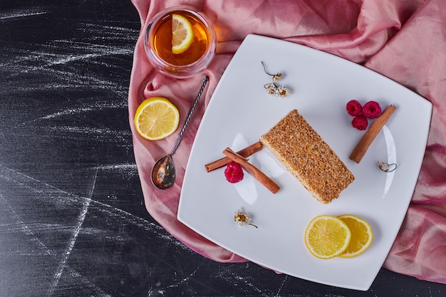 Free photo honey cake on white plate with cinnamon, lemon and berries next to teacup.