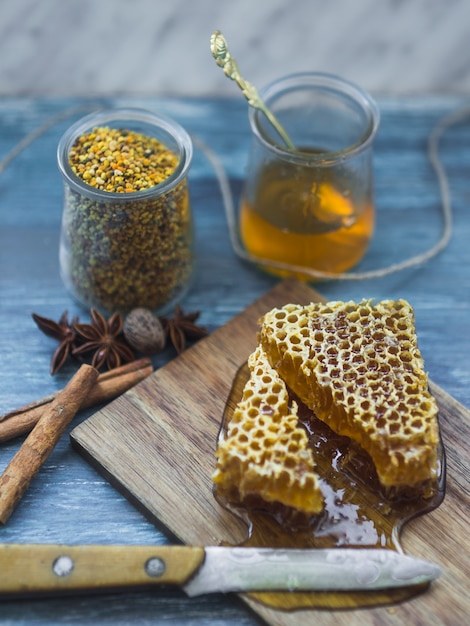 Honey comb pieces with spices; bee pollens jar and knife on backdrop