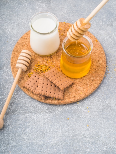 Honey dipper in the honey pot with milk pot and biscuits on coaster