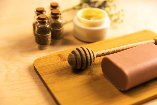 Honey dipper and soap on wooden board with aroma oils and moisturizing cream