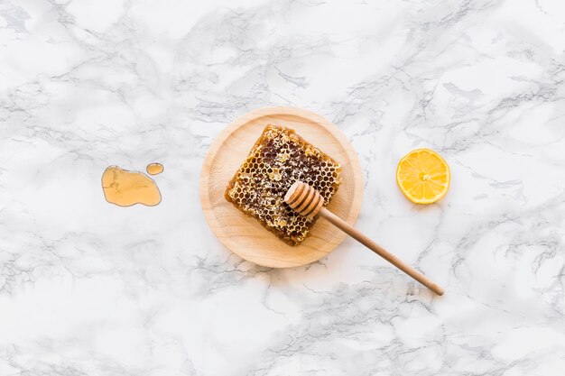 Honey dipper with honeycomb and lemon slice on white marble background