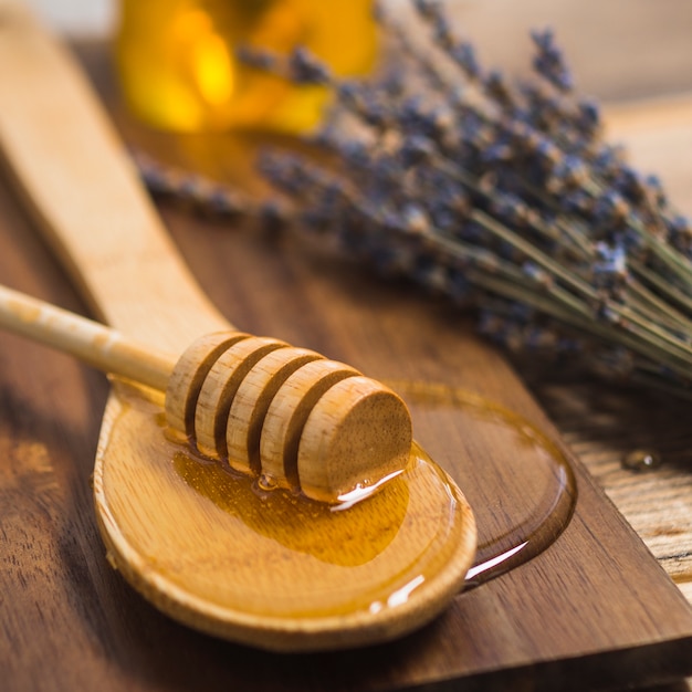 Honey dipper on wooden spoon with honey over chopping board