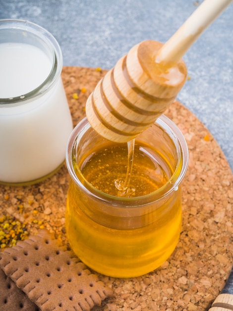 Free photo honey dripping from dripper in glass pot with milk and biscuits on cork coaster