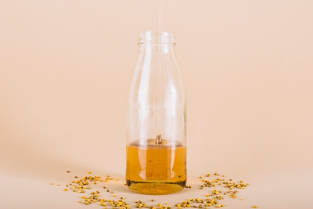Honey dripping in glass bottle with bee pollen on peach colored background