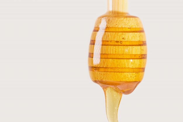 밝은 베이지색 배경에 있는 나무 꿀 스틱 클로즈업에서 꿀이 떨어집니다. 터키 농장의 천연 제품