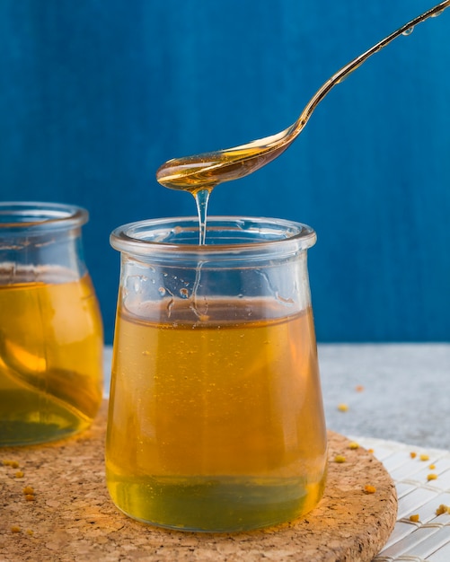 Honey flowing front spoon in glass pot over the coaster