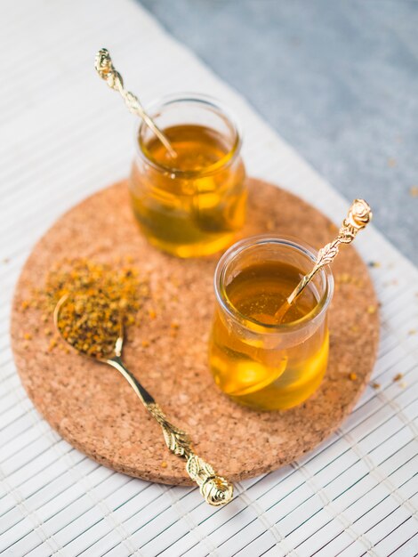 Honey glass pots with spoon and bee pollen on cork coasters