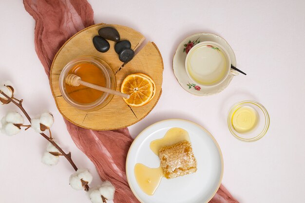 Honey jar; dried citrus slices; la stones; honey comb and cotton branch on white backdrop