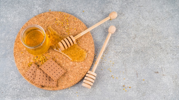 Foto gratuita vaso di miele; polline d'api; biscotti e merluzzo miele sul sottobicchiere sullo sfondo concreto