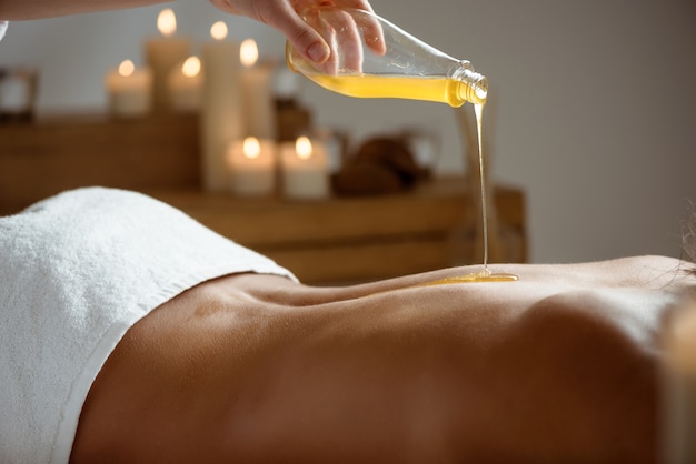 Honey pouring on woman's naked back in spa salon.